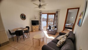 Ein Wohnzimmer mit Sofa, einem Esstisch mit Stühlen, einem Fernseher und einem Deckenventilator.