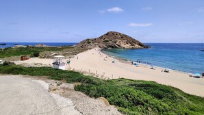 Une plage avec une colline rocheuse, un ciel bleu clair et une mer calme.