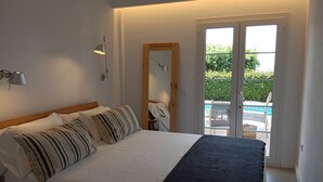Une chambre avec un lit, une lampe de chevet, un miroir et une vue sur l’espace extérieur abritant une piscine.