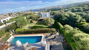 Un espace piscine aménagé sur le toit, avec des chaises longues et une vue sur une ville côtière.