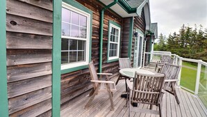 Une terrasse en bois avec une table et des chaises, une rambarde et une fenêtre.