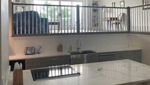 Een moderne keuken met een groot kookeiland, een eethoek met stoelen en uitzicht op de omgeving door grote ramen.