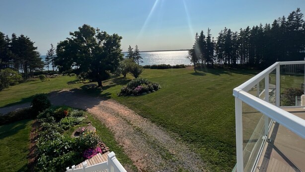 Une vue depuis un balcon donnant sur un espace verdoyant, avec un plan d’eau, des arbres et un ciel dégagé.