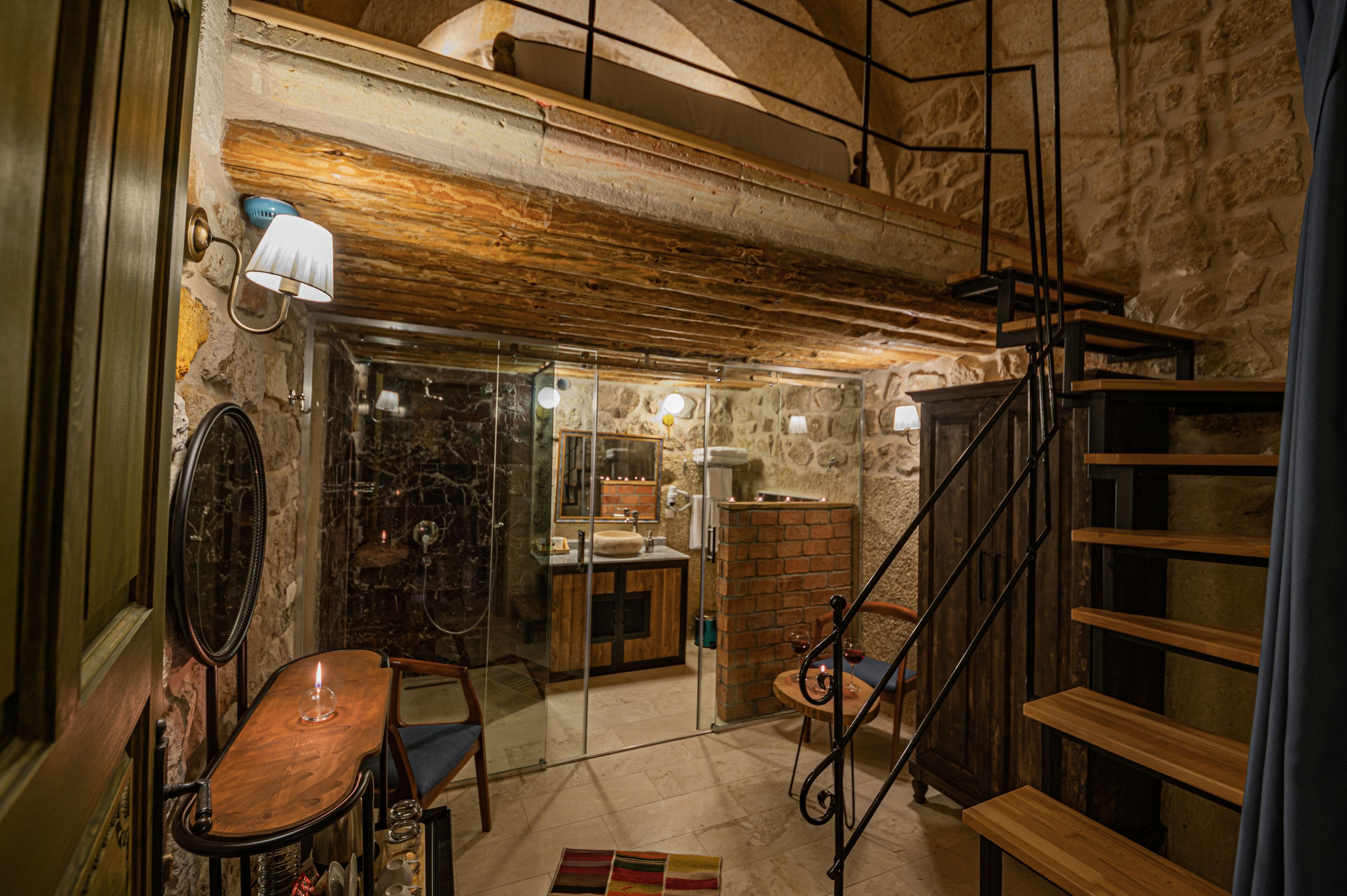 Un interior rústico con pared de piedra, escalera de madera y un pequeño comedor con mesa y sillas.