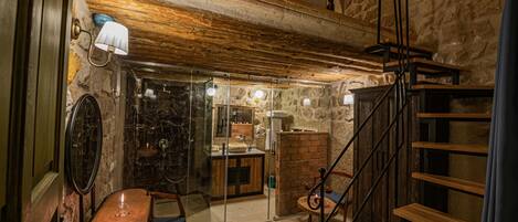 Un interior rústico con pared de piedra, escalera de madera y un pequeño comedor con mesa y sillas.
