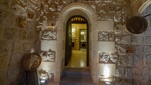 A stone corridor with an arched doorway leading to a room. There are baskets on the floor and a woven basket on the wall. - Janus Cappadocia Hotel (Ürgüp)