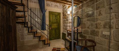 Un interior rústico con una escalera de madera, paredes de piedra, una puerta verde y una pequeña mesa con copas de vino.