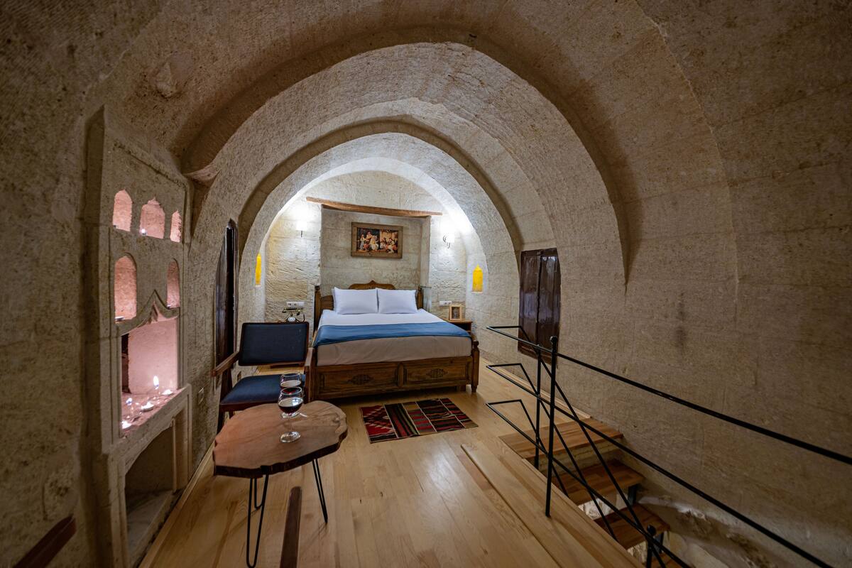 A room with a wooden bed, a small table with a glass, and a chair.