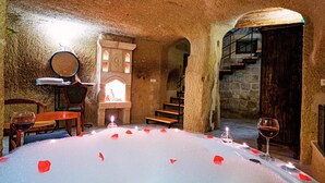 A cozy, candle-lit room with a stone interior, a wooden staircase, and a table set with rose petals and wine glasses. - Janus Cappadocia Hotel (Ürgüp)