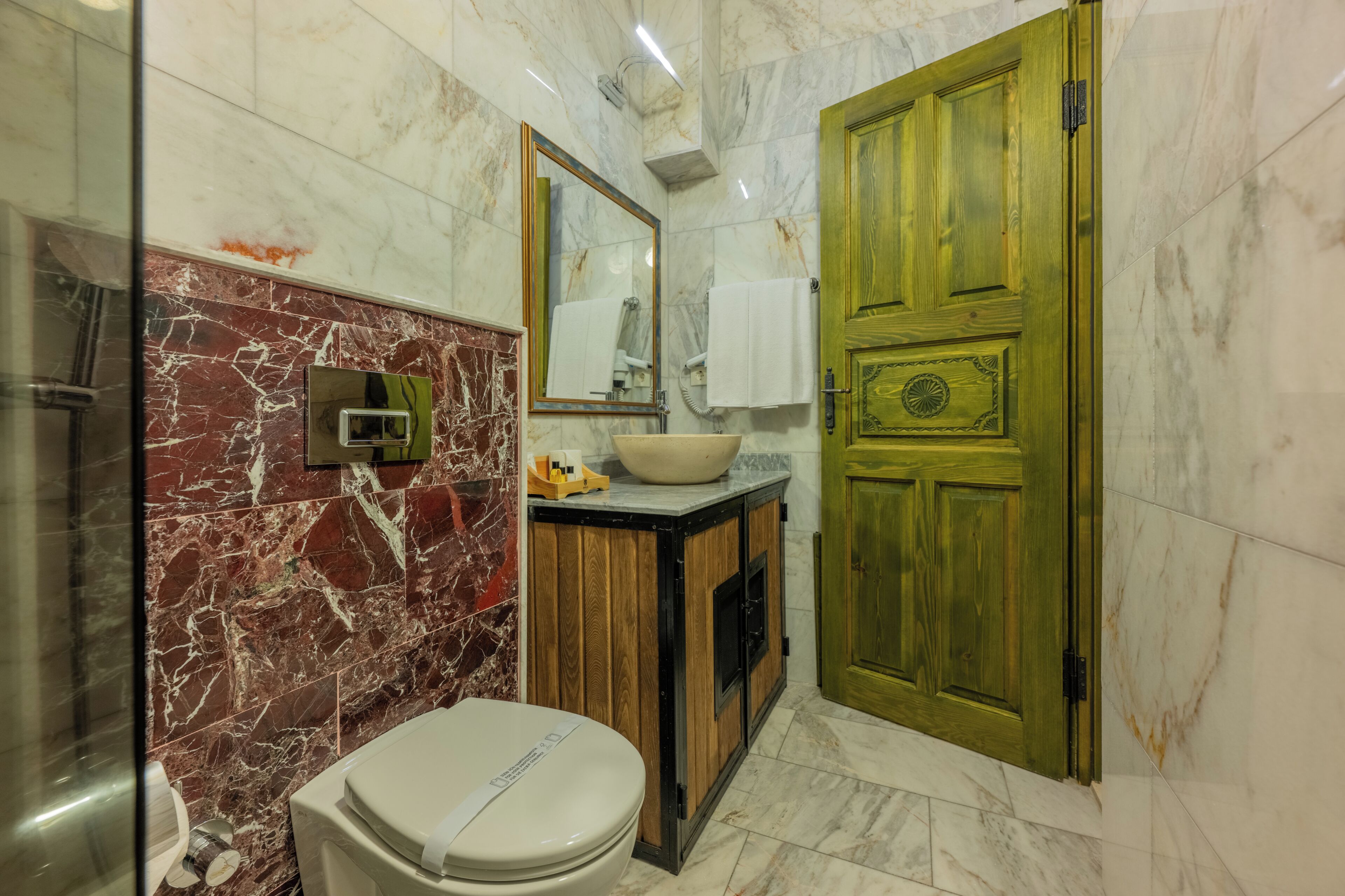 A bathroom with a marble wall, a wooden vanity, a toilet, and a green door.