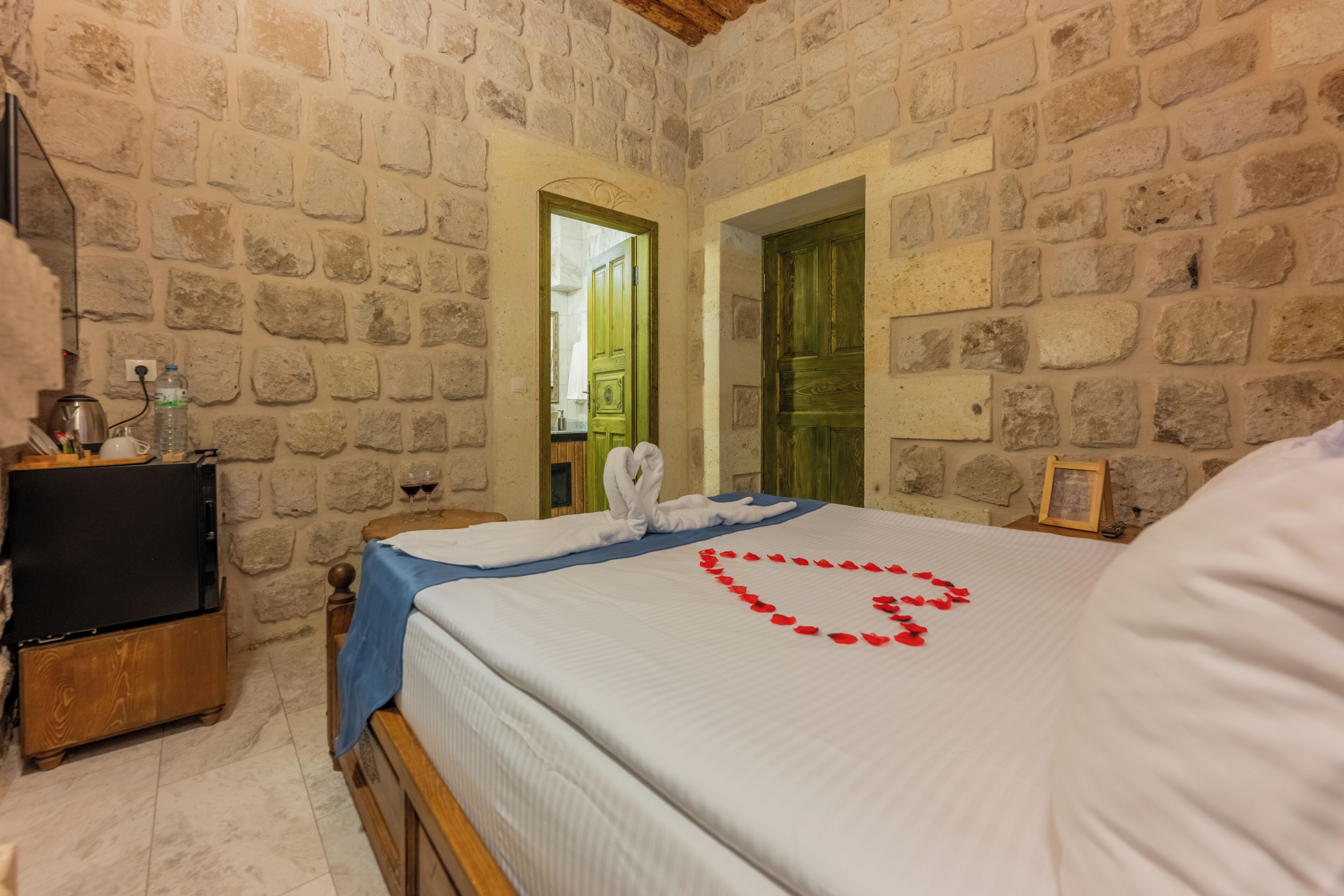 A stone-walled room with a bed, a wooden nightstand, and a framed picture.