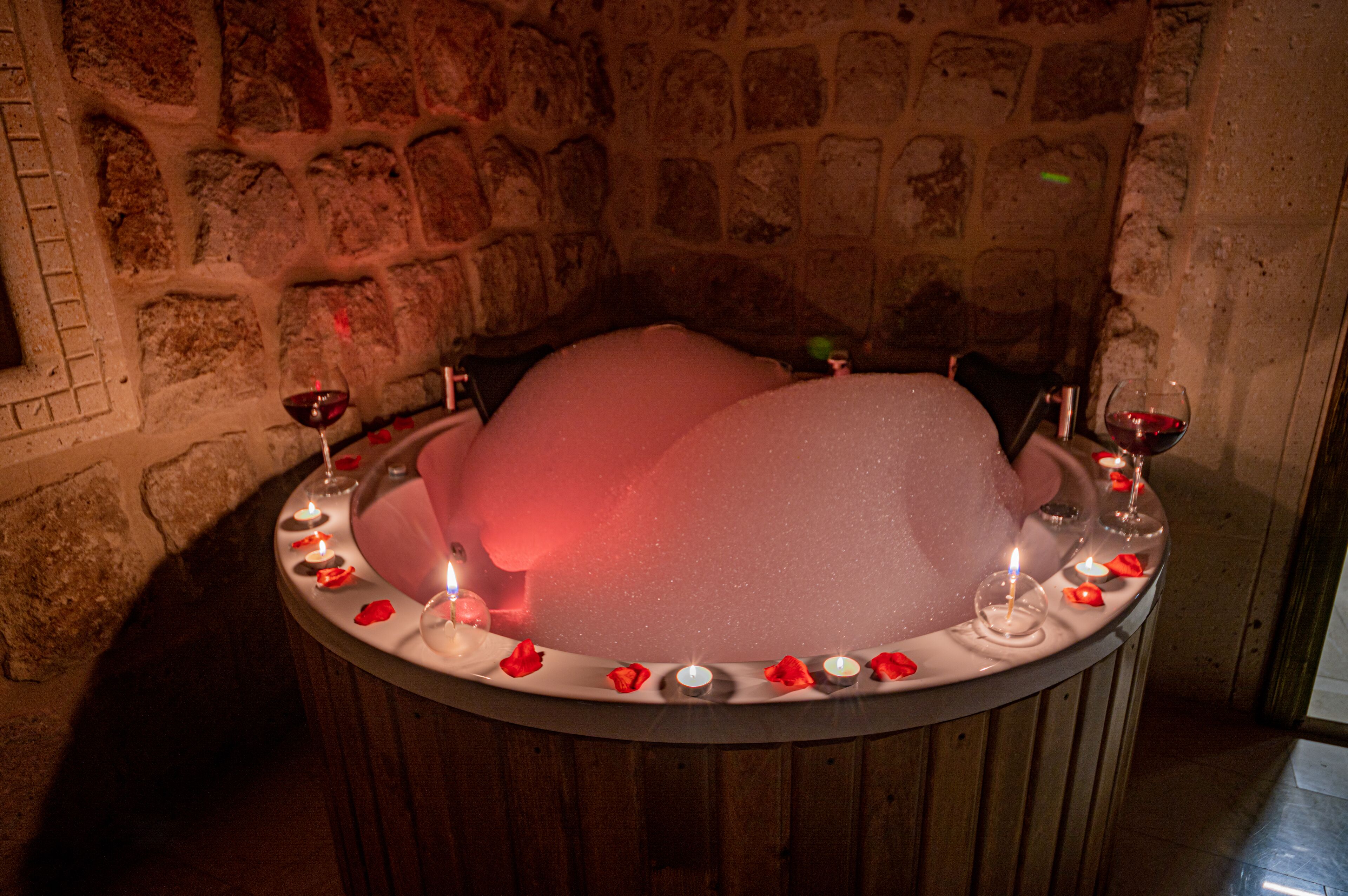 Una habitación de paredes de piedra con una bañera redonda rodeada de velas y pétalos de rosa.