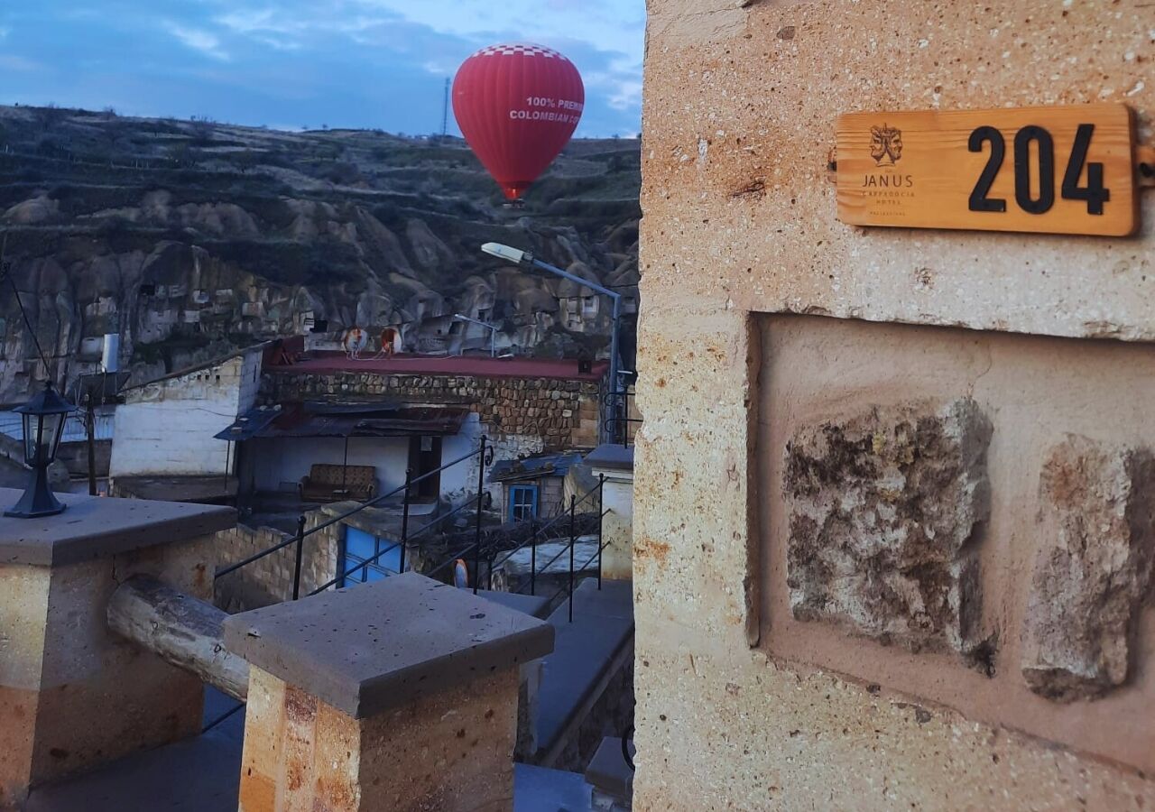 Une vue d’une ville avec, au loin, un ballon à air chaud rouge, un bâtiment en pierre avec une enseigne en bois portant le numéro 204, et un escalier menant à un niveau supérieur.