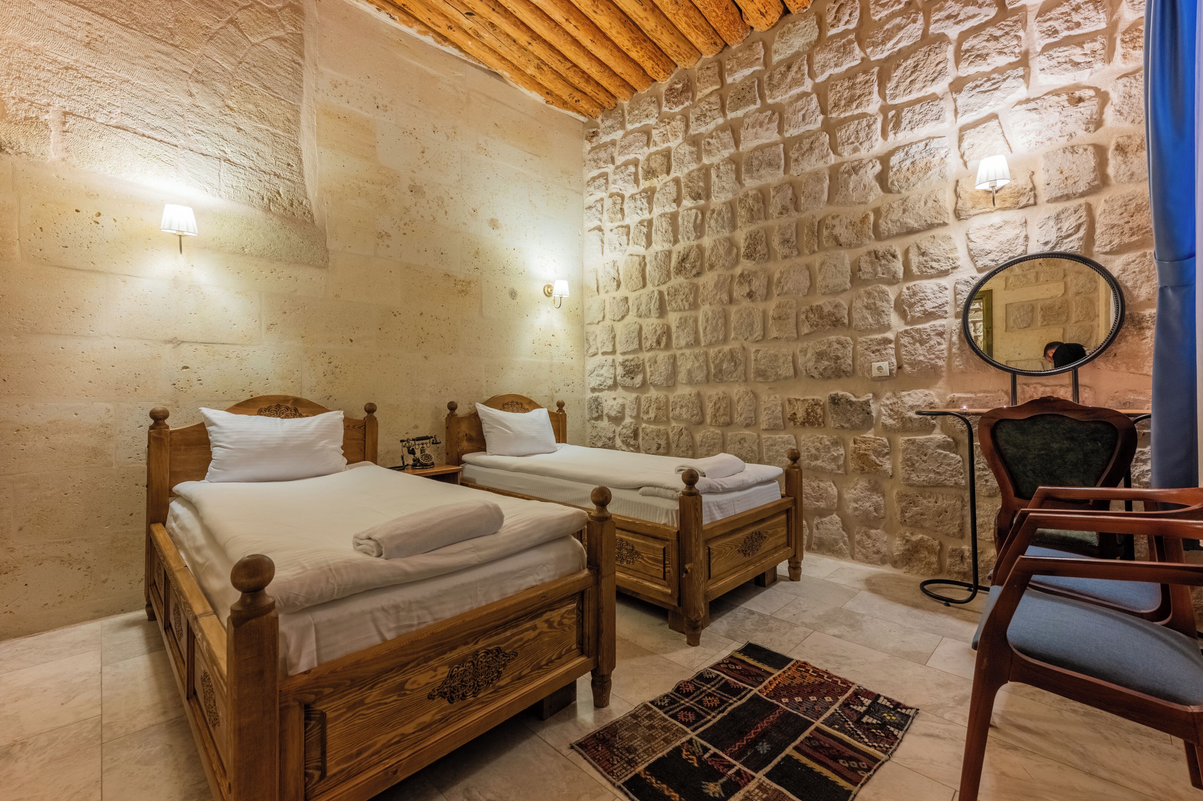 A room with two wooden beds, a stone wall, a mirror, and a chair.