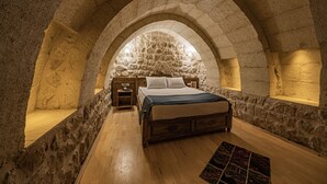 A bedroom with a stone arched ceiling, a wooden bed, and a nightstand with a lamp. - Janus Cappadocia Hotel (Ürgüp)