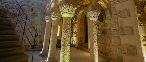 A stone building with a staircase leading to an upper level, featuring ornate columns and a wooden ceiling.