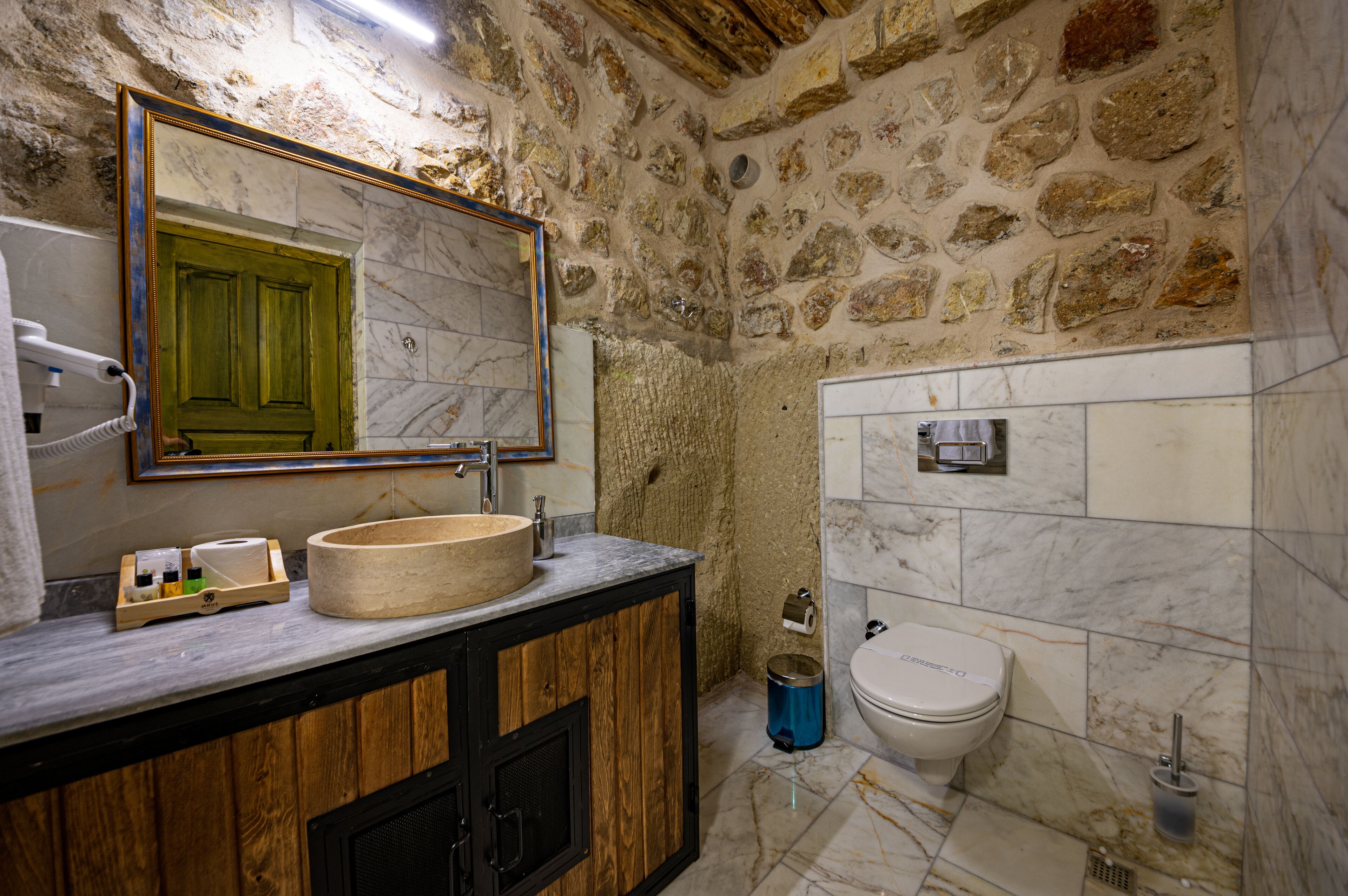 A bathroom with a stone wall, a wooden vanity, a marble sink, and a toilet.