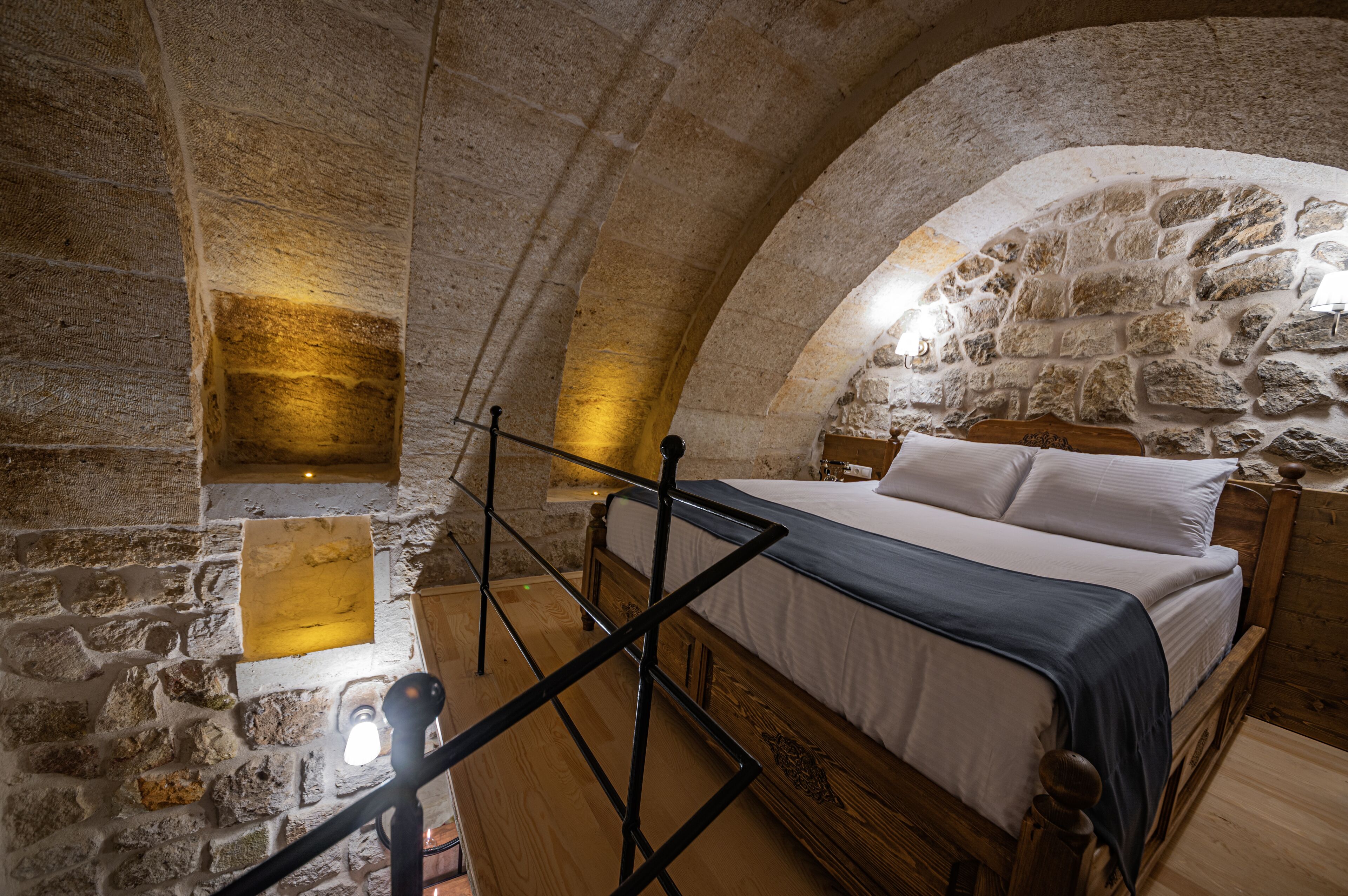 Un dormitorio con paredes de piedra, una cama de madera, una ventana pequeña y una escalera de madera.