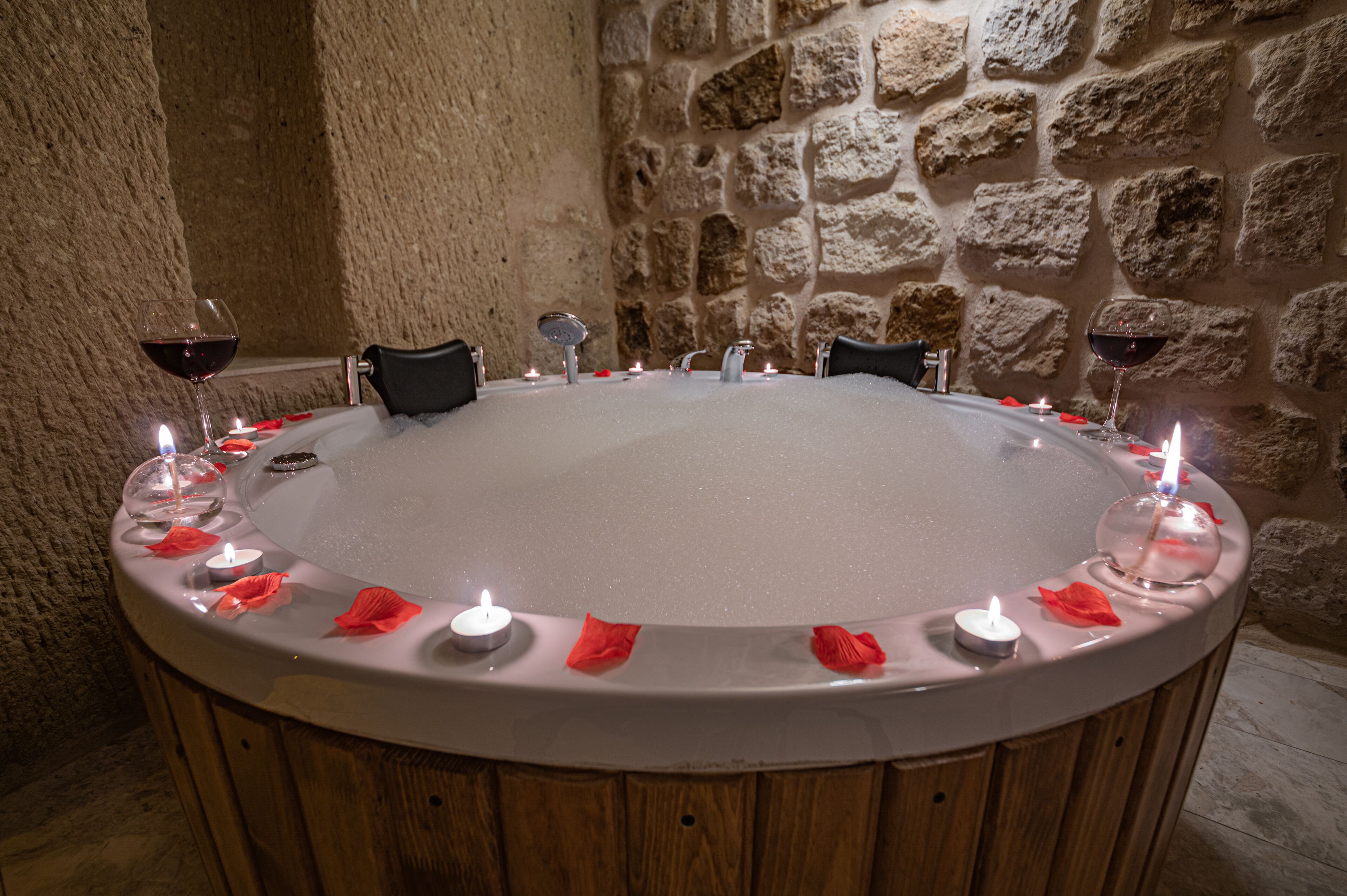 A round hot tub with candles and red flowers, surrounded by stone walls.