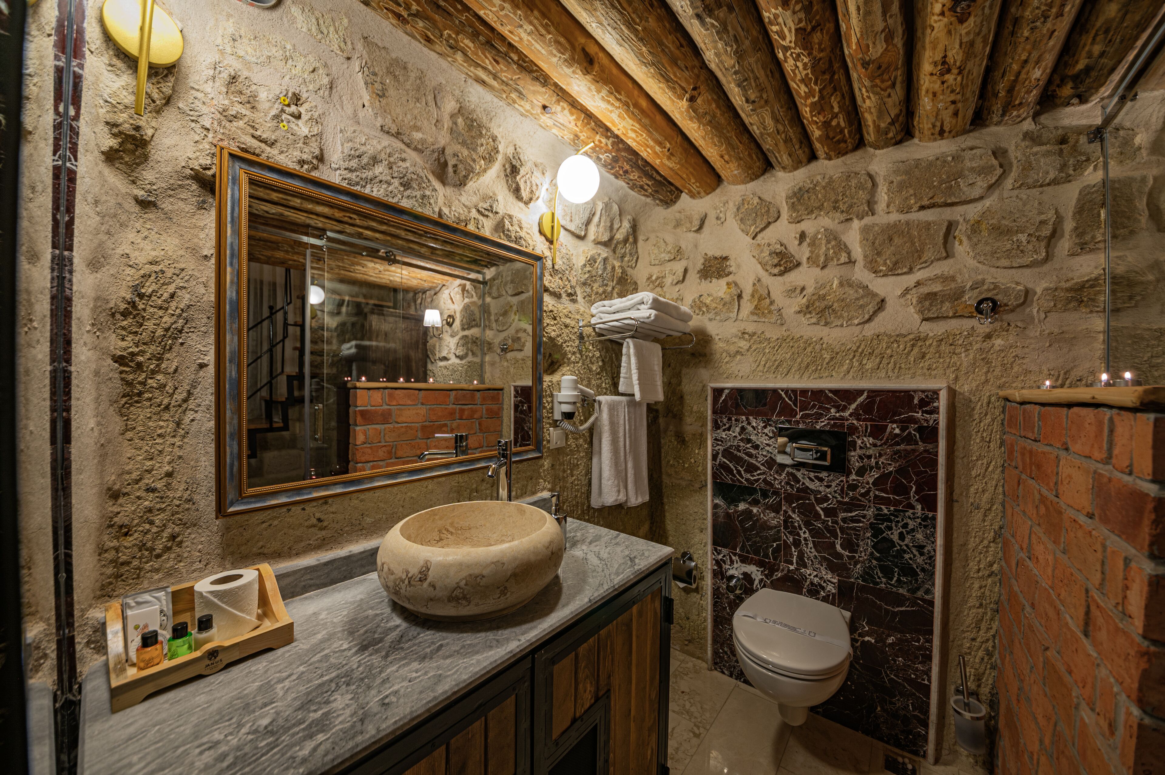 Un baño rústico con pared de piedra, techo de madera, lavabo de mármol y retrete.