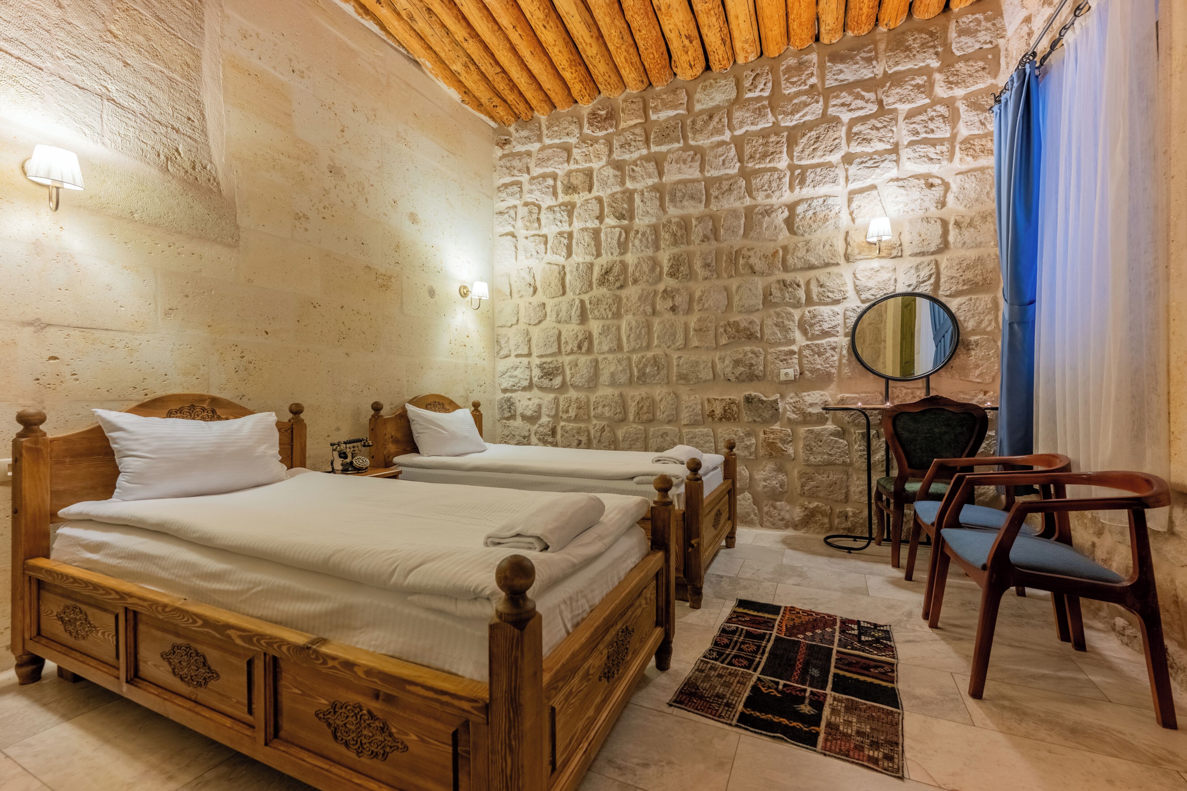 A room with two wooden beds, a stone wall, a mirror, and a blue curtain.