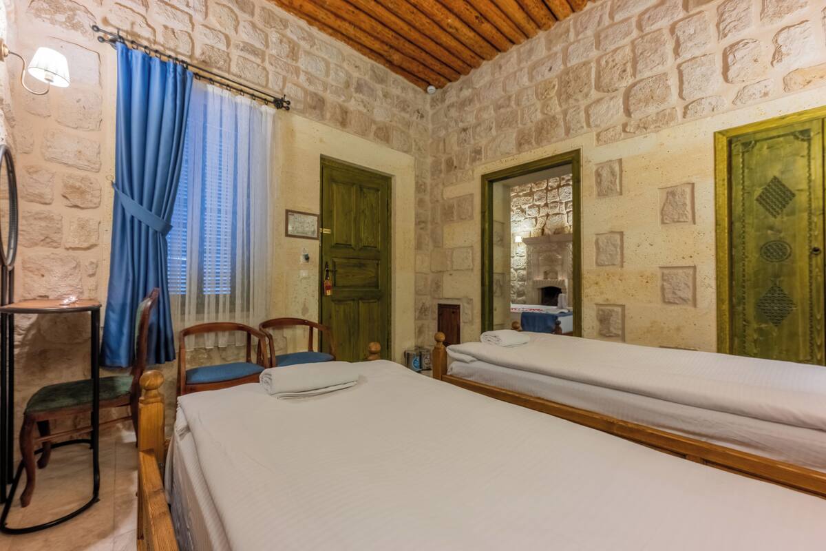 A room with two beds, a chair, a table, and a stone wall.