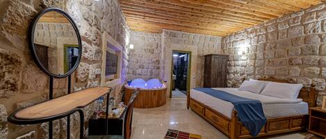 Una habitación con paredes de piedra y techo de madera, con una cama, una silla, un escritorio y una bañera con luces.