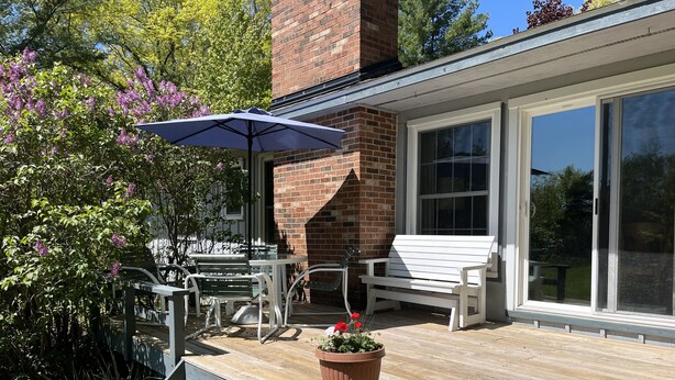 A wooden deck with outdoor furniture, a brick chimney, and a large sliding glass door. - Sunrise Side Retreat - Sleeps 7 (Harrisville)