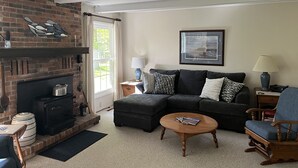 A living room with a brick fireplace, a black sofa, a wooden coffee table, and a blue armchair. - Sunrise Side Retreat - Sleeps 7 (Harrisville)