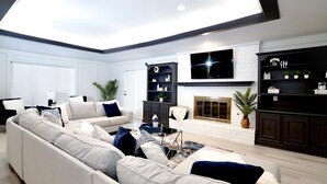 Ein modernes Wohnzimmer mit einer Eckcouch, einem Kamin, einem an der Wand befestigten Fernseher und integrierten Regalen mit Dekorationselementen.