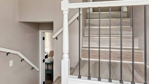 Een trap met een witte leuning en zwarte spijbels, die uitkomt op een plateau met een deur.