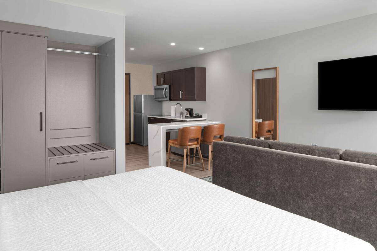 Ein modernes Hotelzimmer mit Bett, Küchenzeile, Sitzecke und Fernseher.