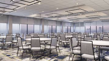 A large conference room with round tables and chairs, a patterned carpet, and a city view through large windows.
