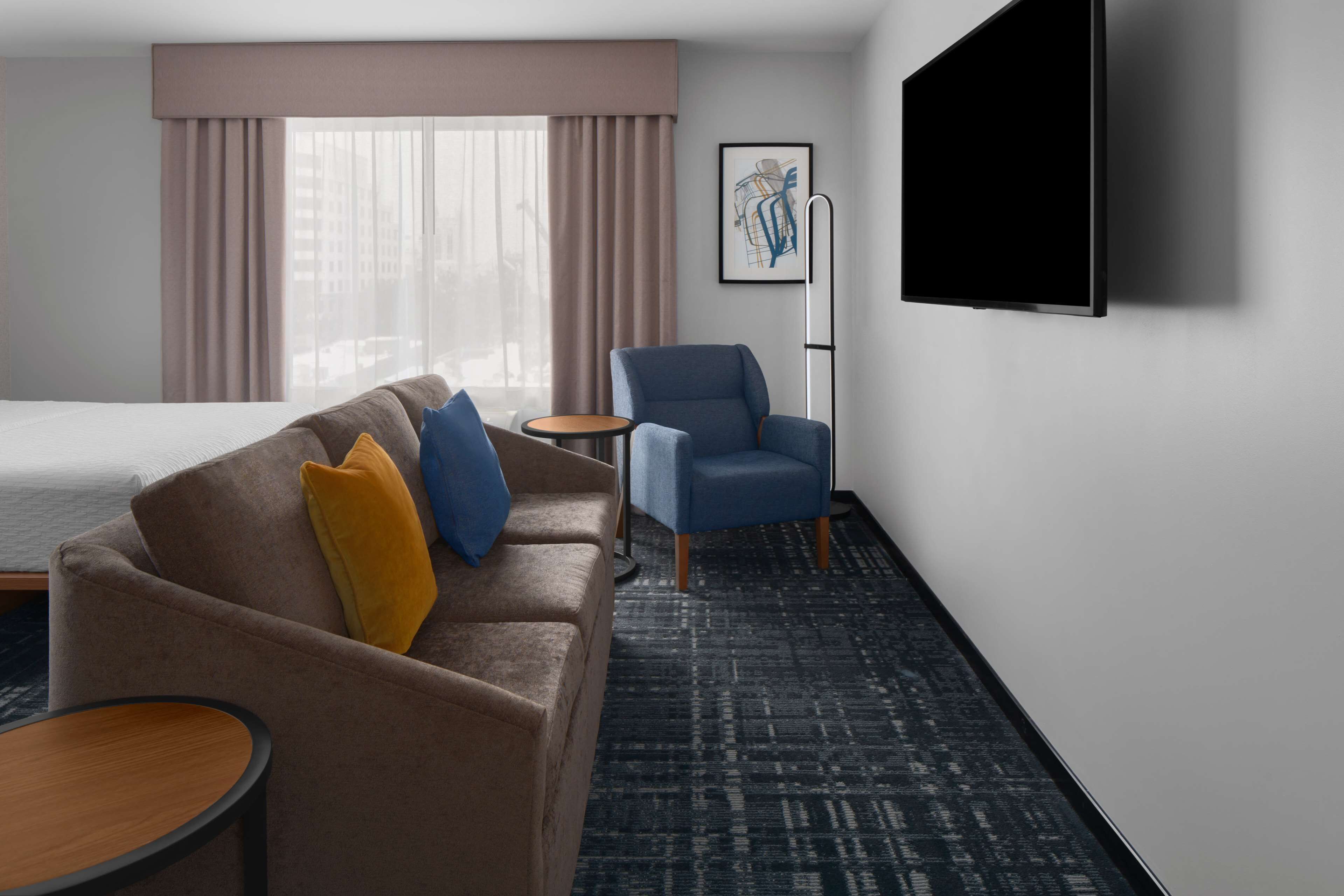 A hotel room with a bed, a sofa, a chair, a small table, and a TV mounted on the wall.