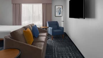 Een hotelkamer met een bed, een slaapbank, een stoel, een kleine tafel en een aan de muur bevestigde televisie.