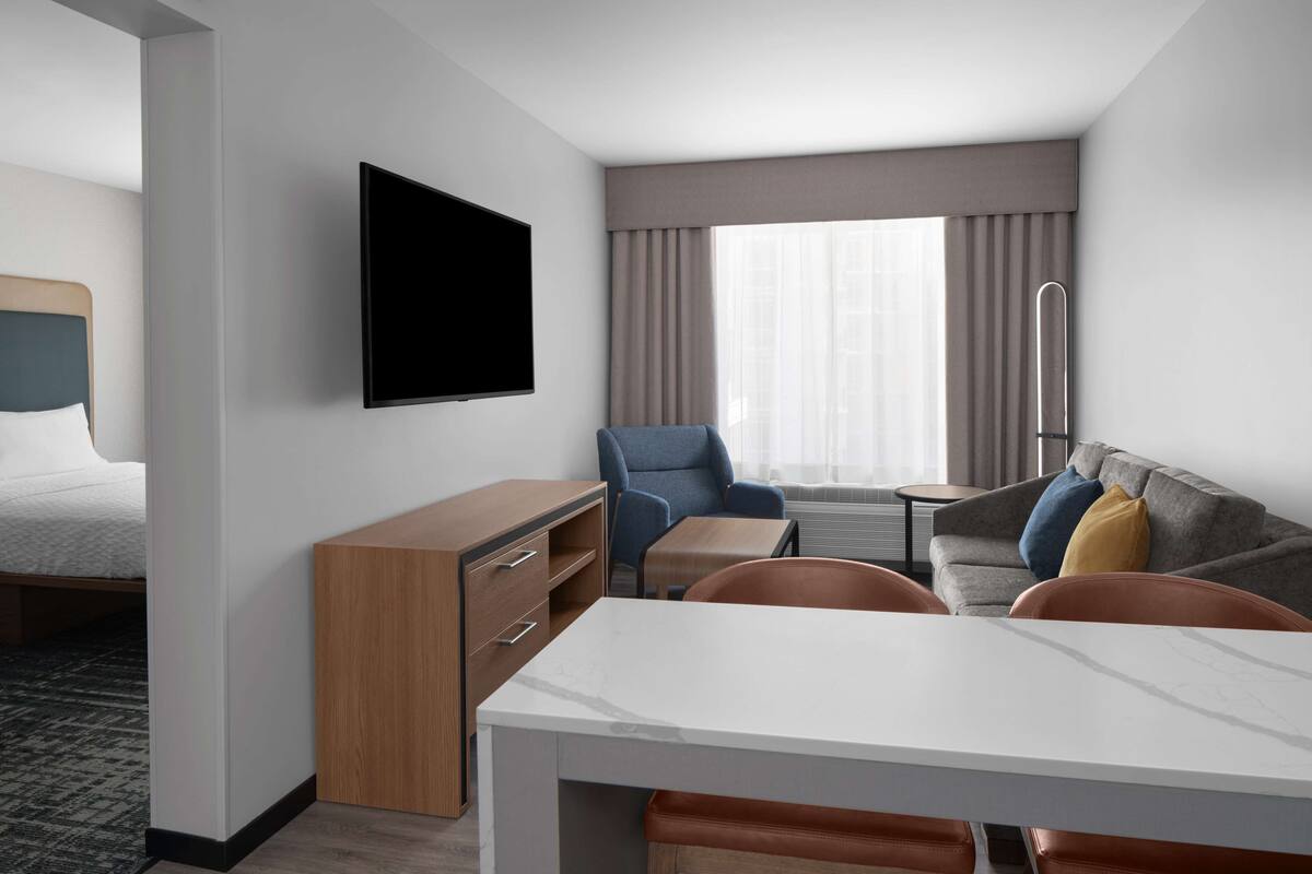 Ein Hotelzimmer mit Bett, Schreibtisch, Stuhl, Sofa, Fernseher und einem Fenster mit Vorhängen.