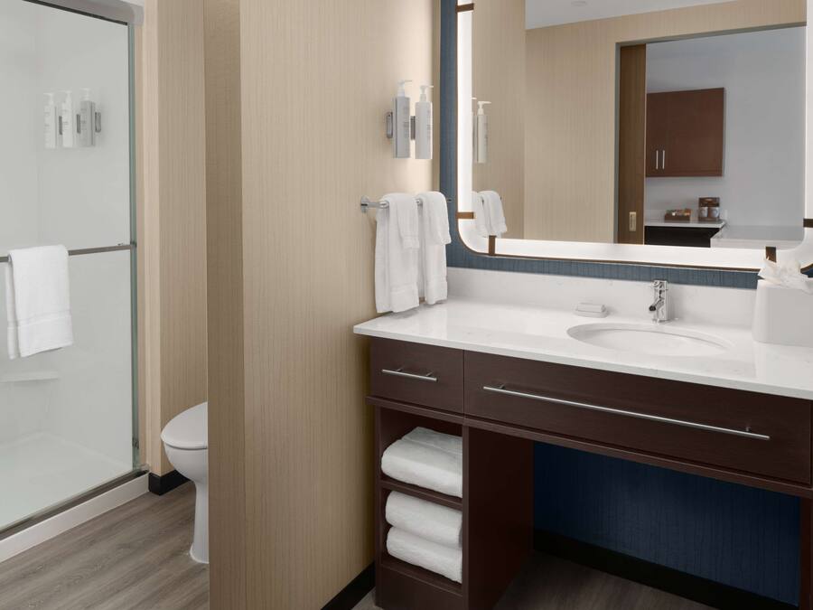 Une salle de bain moderne avec une douche à parois de verre, des toilettes blanches, un meuble-lavabo avec un évier et un porte-serviettes, et un grand miroir.