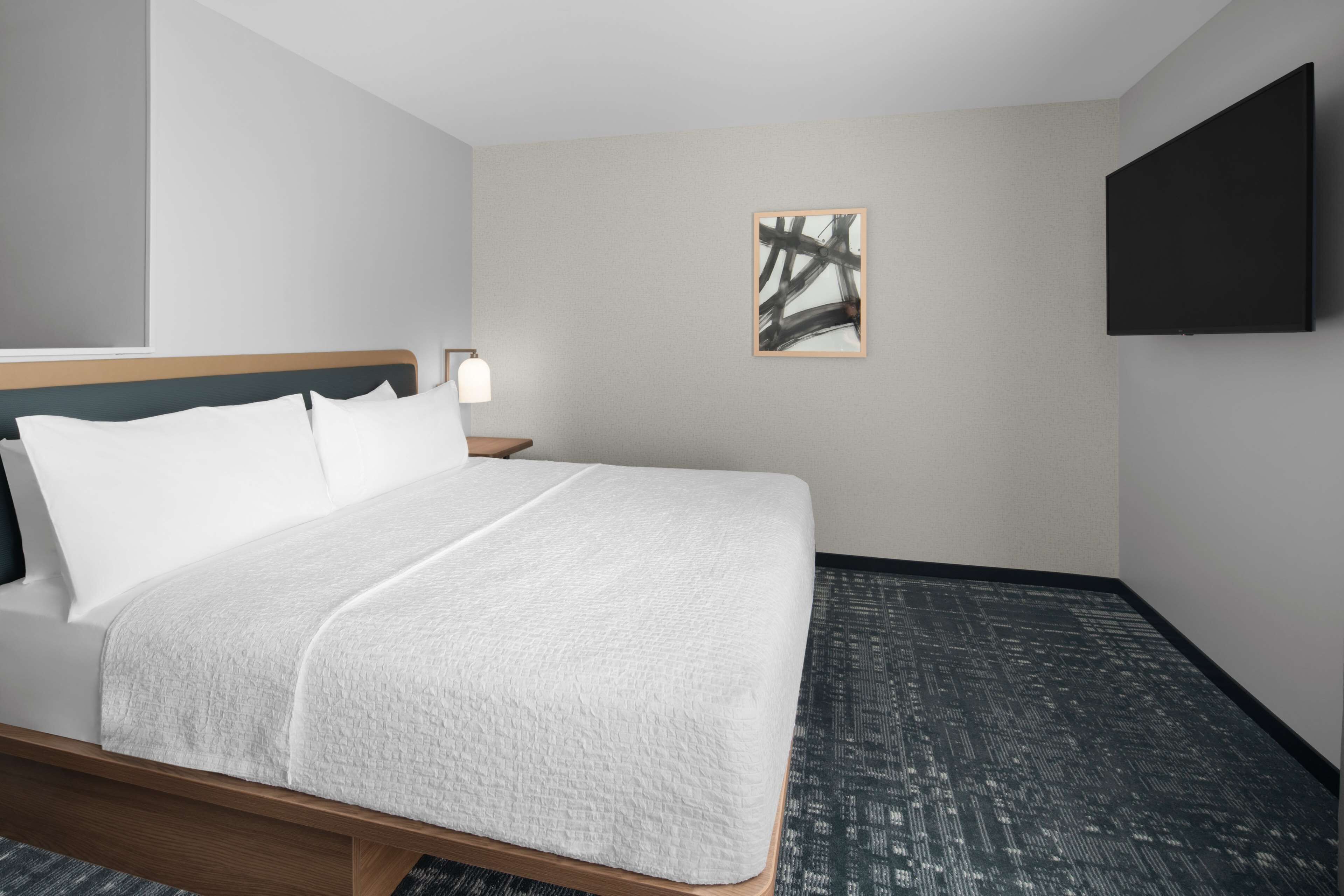 A hotel room with a bed, a nightstand, a wall-mounted TV, and a painting.