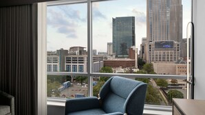 Une chambre d’hôtel dotée d’une grande fenêtre donnant sur la ville, d’un fauteuil bleu et d’une petite table.