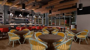 Un espace bar moderne doté de différents types de sièges, notamment des tables et des chaises rondes, ainsi que d’un comptoir avec des étagères remplies de bouteilles.