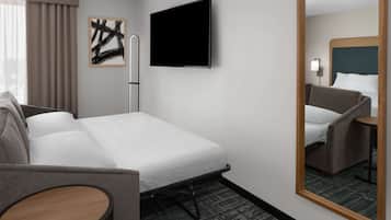 Une chambre d’hôtel comprenant un lit, une chaise, une petite table, un téléviseur à écran plat et un miroir.