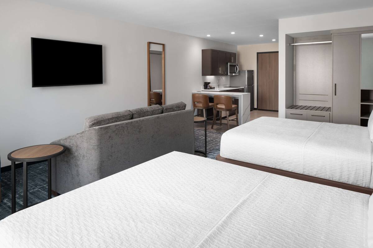 Ein Hotelzimmer mit zwei Betten, einem Schlafsofa, einem Schreibtisch mit Stühlen, einer Mikrowelle und einem Kleiderschrank.