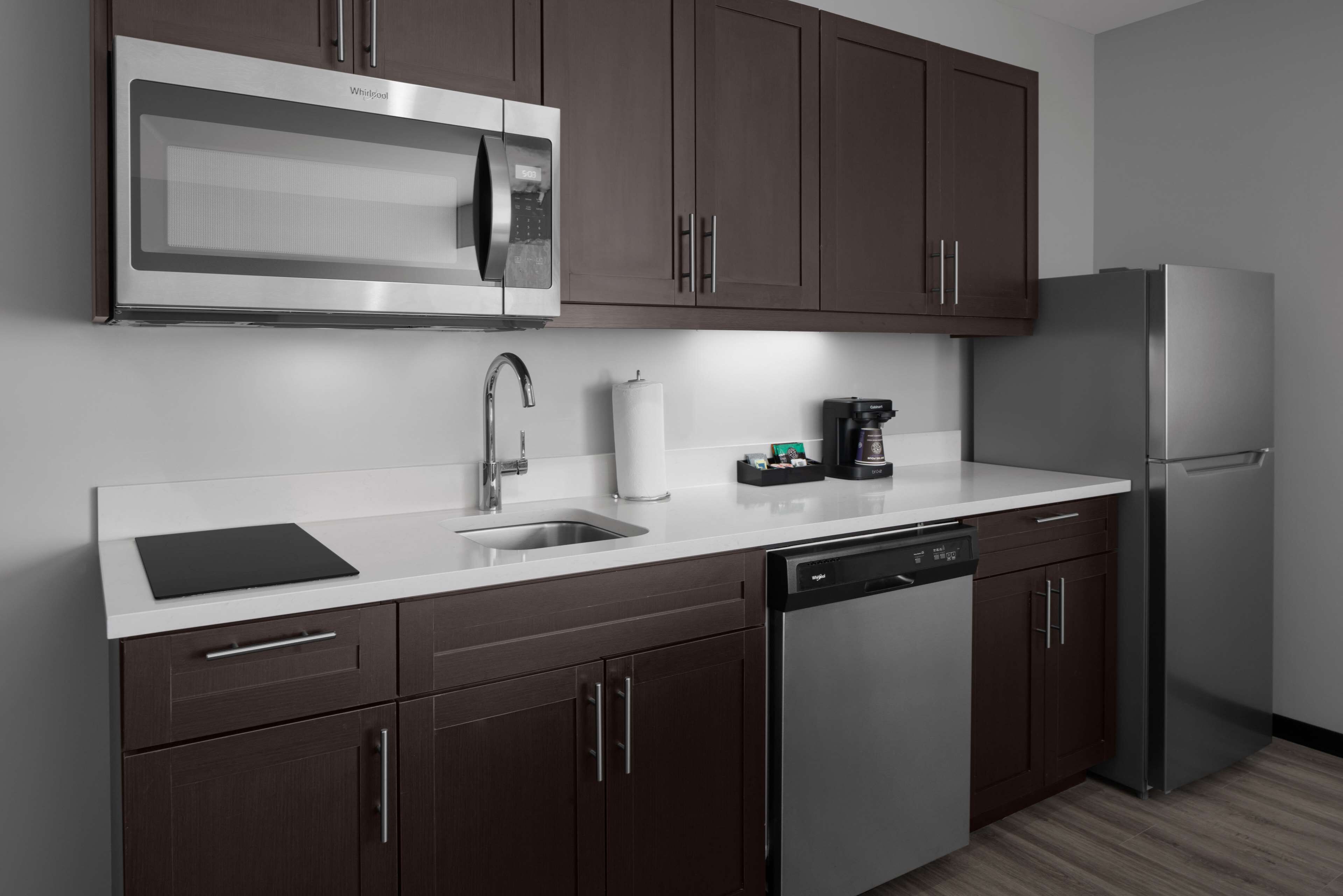 A modern kitchen with dark brown cabinets, stainless steel appliances, a dishwasher, and a coffee maker.