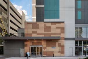 Ein modernes Gebäude mit einer Fassade aus Holz und Beton, ein Schild mit der Aufschrift "Homewood Suites" und einem wolkenlosen Himmel im Hintergrund.
