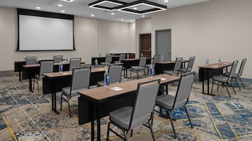 A conference room with multiple tables and chairs, a projector screen, and a carpeted floor.