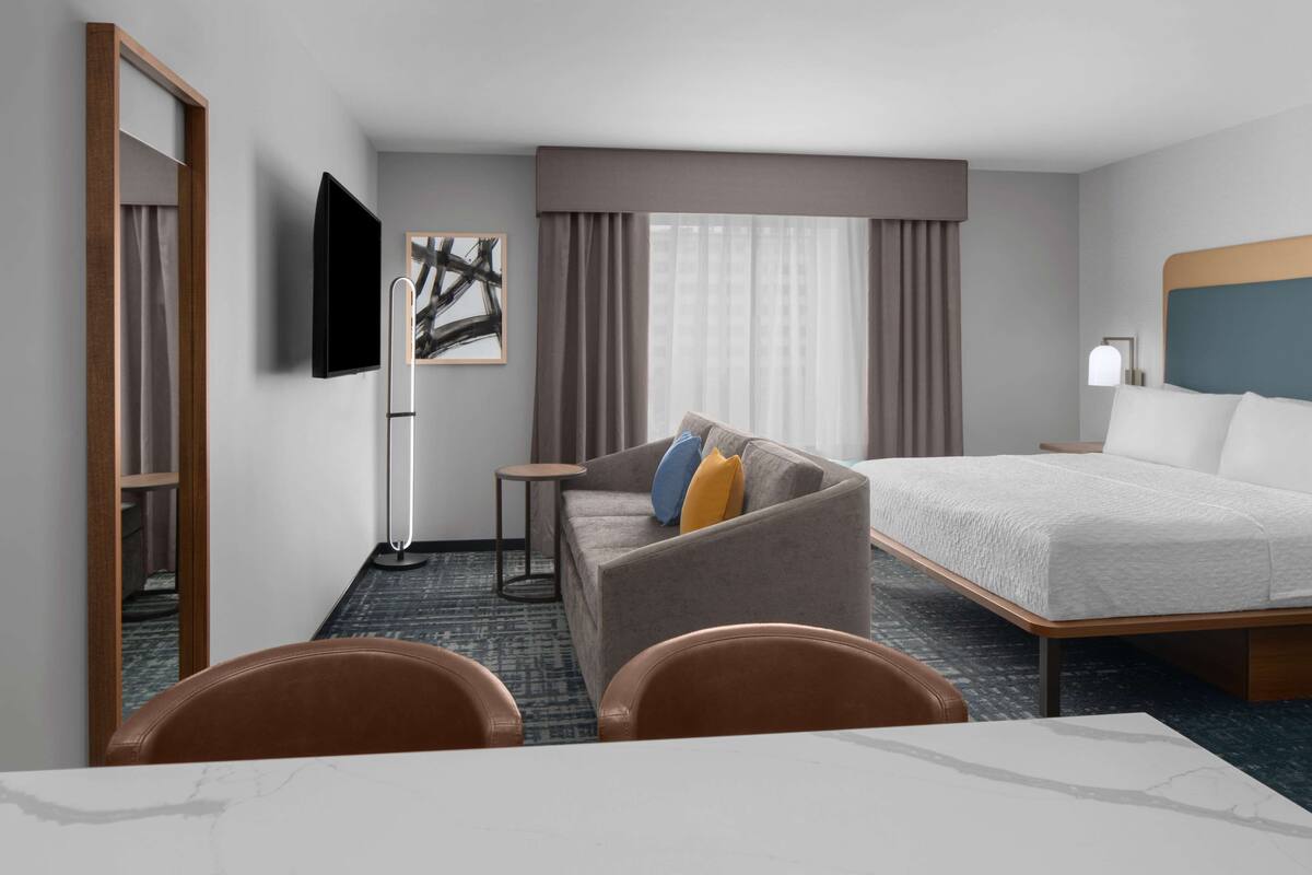 Ein Hotelzimmer mit Bett, Sofa, Fernseher und Schreibtisch mit Stühlen.