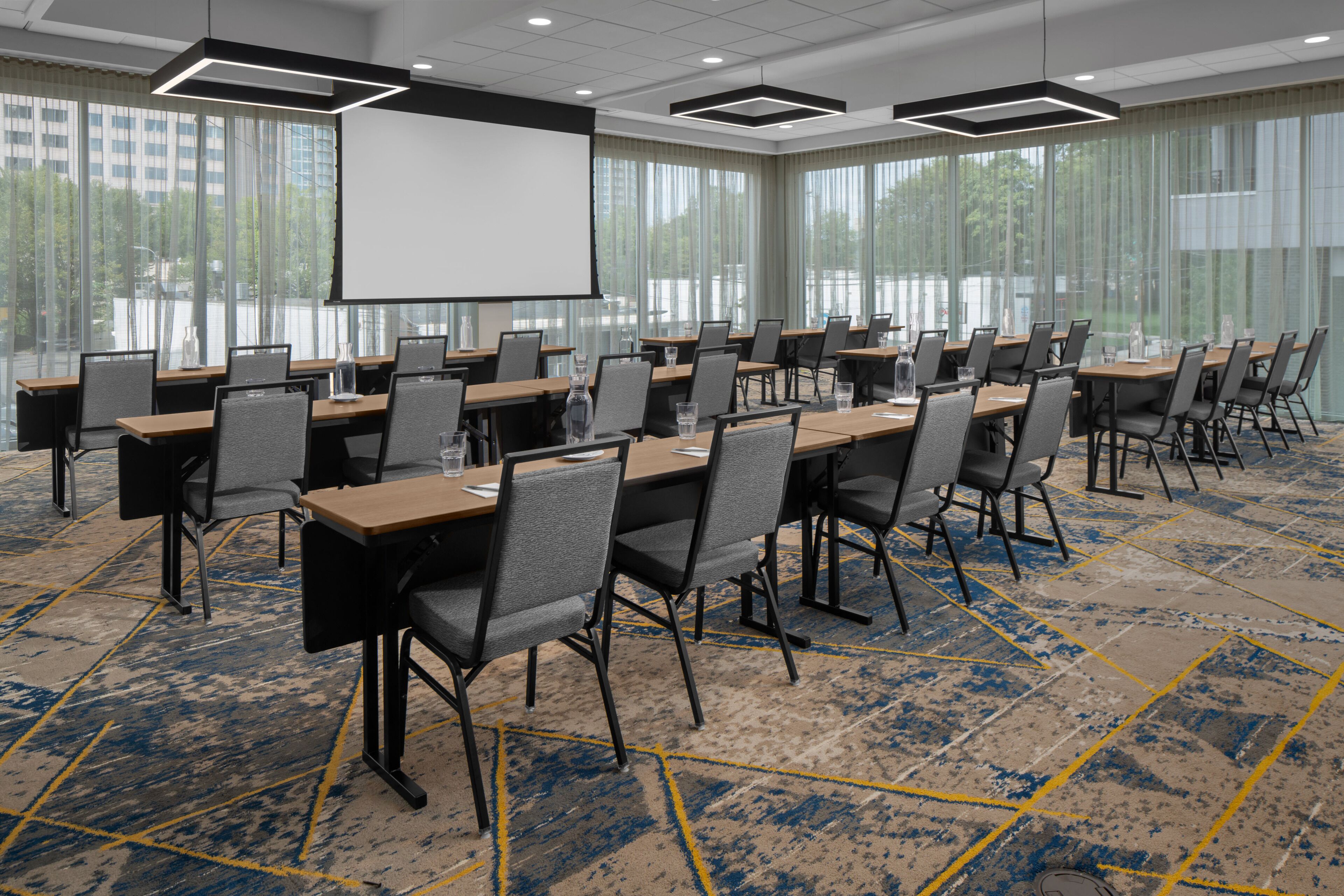 A conference room with multiple tables and chairs, large windows, and a projector screen.