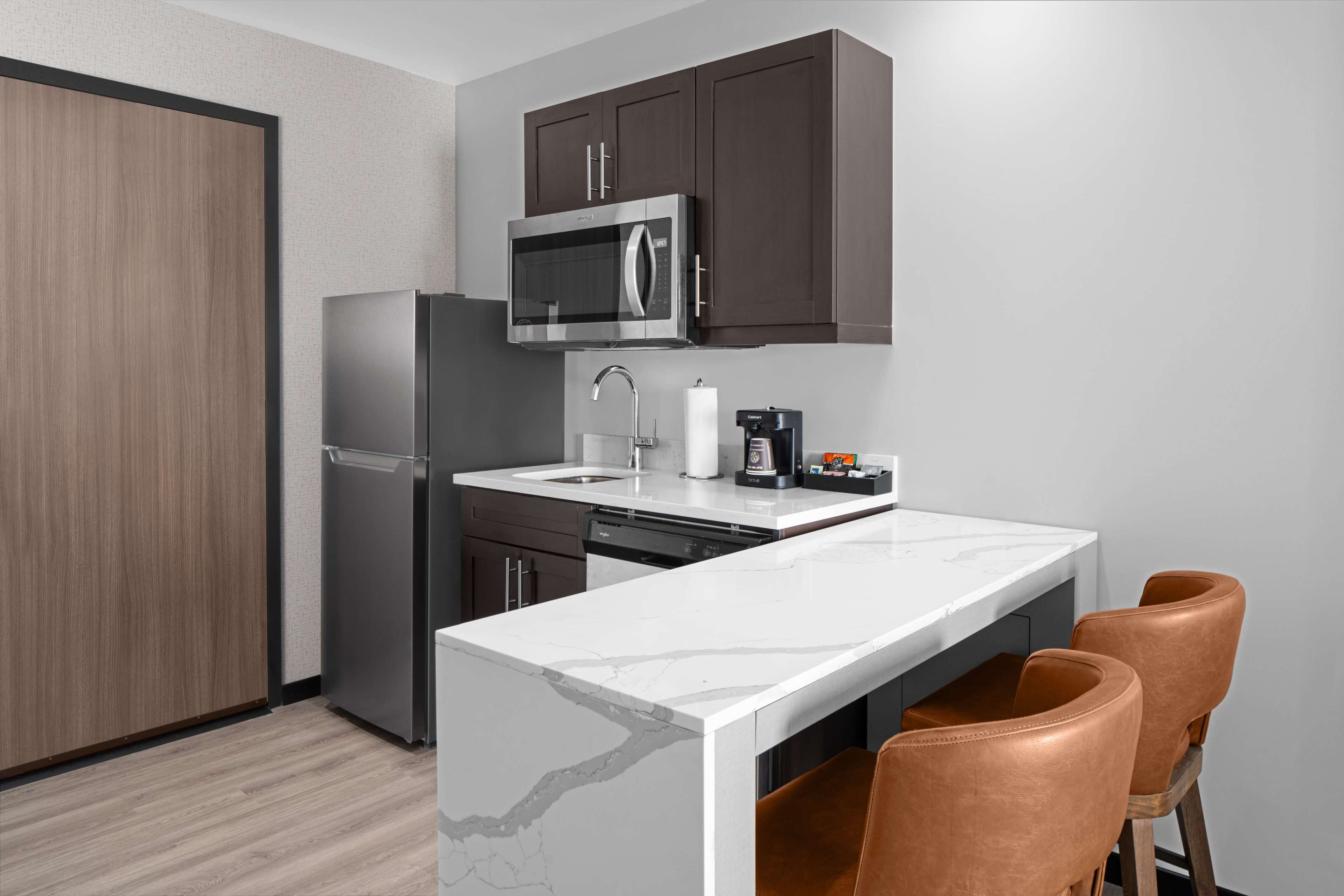 A compact kitchen with a microwave, refrigerator, and a small island with chairs.