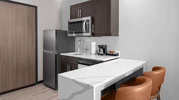 A compact kitchen with a microwave, refrigerator, and a small island with chairs.