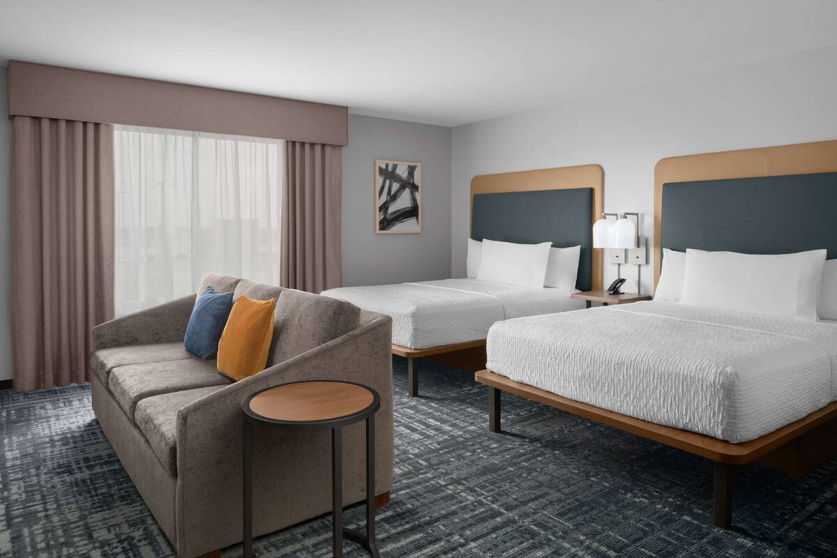 Ein Hotelzimmer mit zwei Betten, einem Sofa, einem kleinen Tisch und einem Fenster mit Vorhängen.